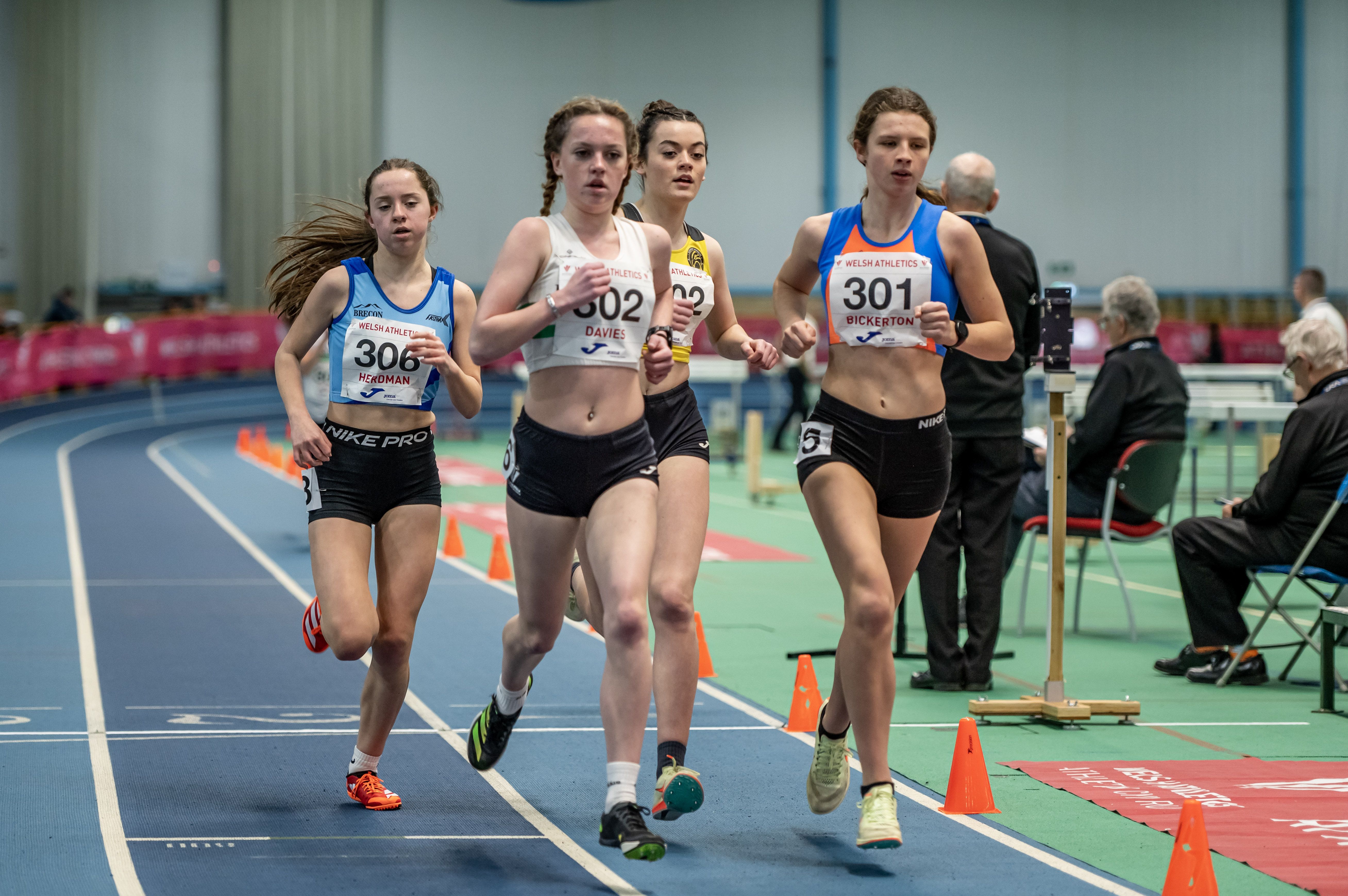 Junior girls athletes competing on an indoor track.